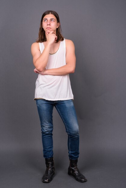 jonge knappe androgyne man met lang haar tegen grijze muur