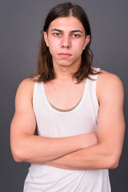 jonge knappe androgyne man met lang haar tegen grijze muur