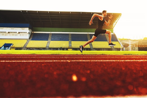 Jonge knappe atleet die bij zonsondergang in het stadion rent Foto van hoge kwaliteit