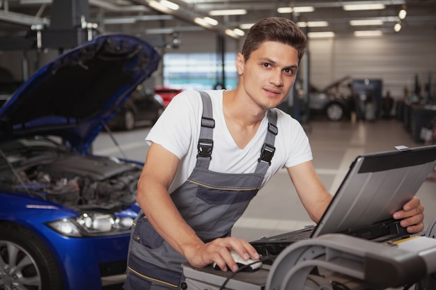 Jonge knappe autowerktuigkundige die voertuig in zijn garage herstelt