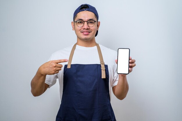Jonge knappe aziatische barista-man met een schort die met de vinger wijst naar het mobiele scherm met app en glimlacht