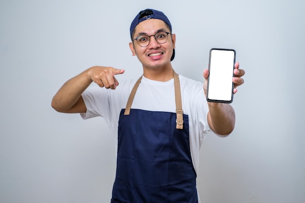 Jonge knappe aziatische barista-man met schort wijzend op mobiel scherm met app en glimlach