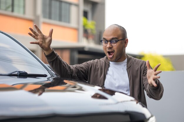 Jonge knappe aziatische man die de nieuwe auto krijgt. Hij is erg blij en opgewonden met de hand in de lucht. Koop of huur autoconcept.