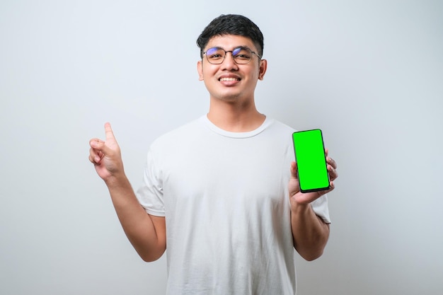 Jonge knappe aziatische man die een leeg scherm van een smartphone toont, erg blij met de hand en de vinger naar de zijkant te wijzen