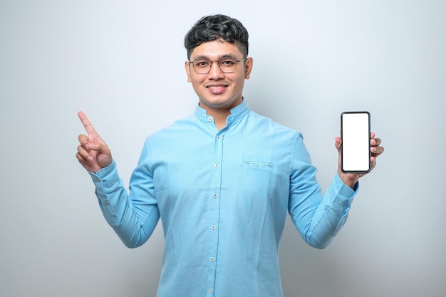 Jonge knappe aziatische man die het scherm van de smartphone laat zien, erg blij met de hand en de vinger naar de zijkant te wijzen