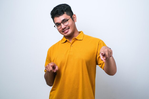 Jonge knappe aziatische man met een casual shirt over een witte achtergrond wijzend naar jou en de camera met vingers die positief en vrolijk glimlachen