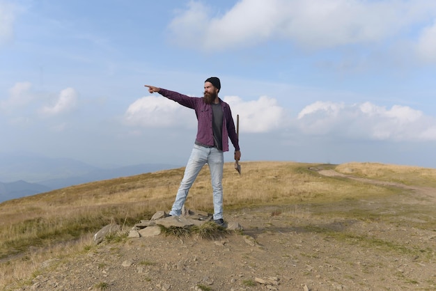 Jonge knappe bebaarde hipster man in geruit hemd met lange baard met bijl of bijl op bergtop op natuurlijke achtergrond met lucht