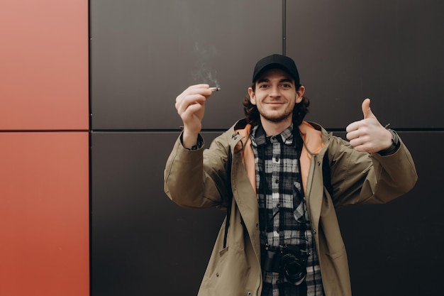 Jonge knappe bebaarde hipster man roken sigaret in de buurt van muur op straat