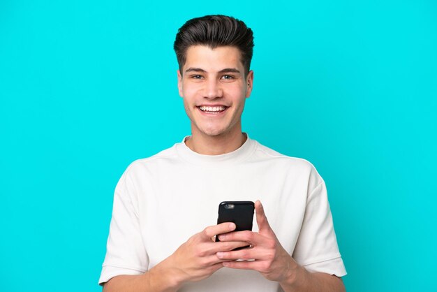 Jonge knappe blanke man geïsoleerd op blauwe achtergrond die een bericht verzendt met de mobiel