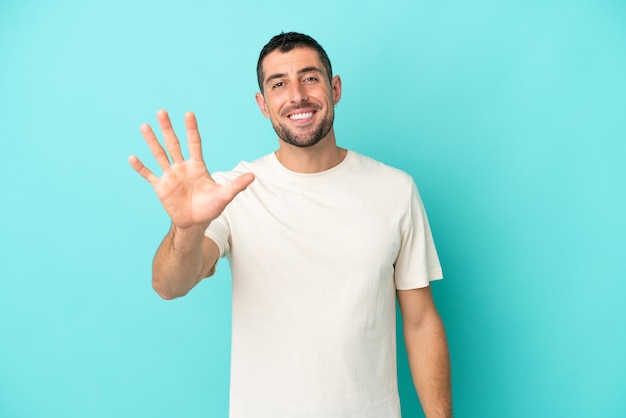 Jonge knappe blanke man geïsoleerd op blauwe achtergrond die vijf met vingers telt
