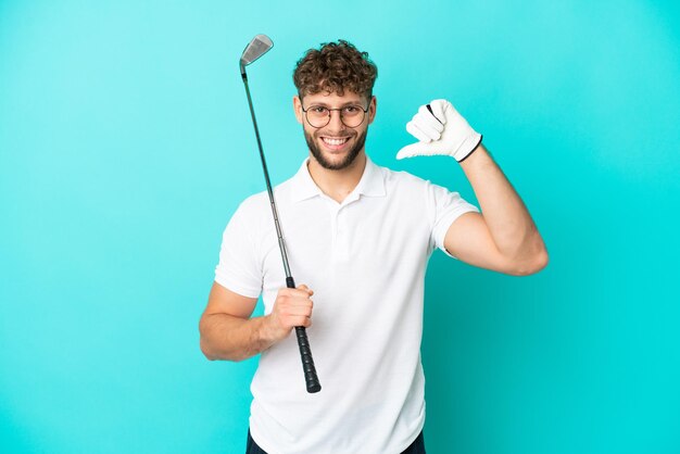 Jonge knappe blanke man geïsoleerd op blauwe achtergrond golfen en trots op zichzelf