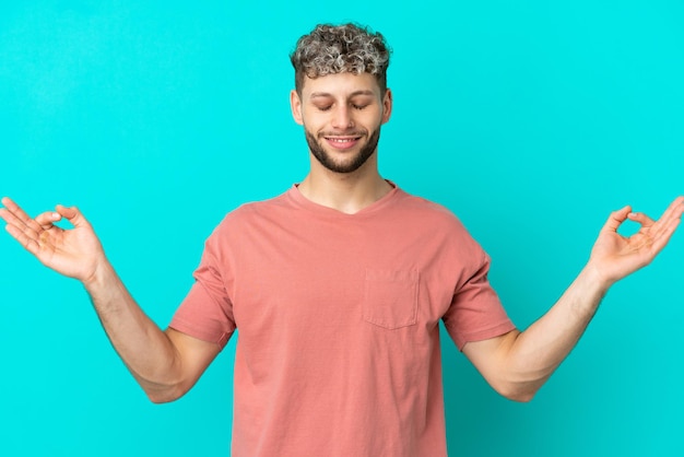 Jonge knappe blanke man geïsoleerd op blauwe achtergrond in zen pose