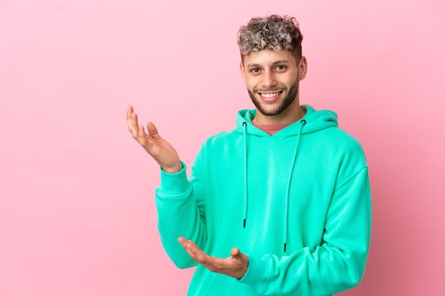 Jonge knappe blanke man geïsoleerd op een roze achtergrond die zijn handen naar de zijkant uitstrekt om uit te nodigen om te komen