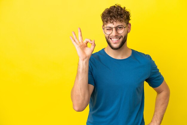 Jonge knappe blanke man geïsoleerd op gele achtergrond met ok teken met vingers