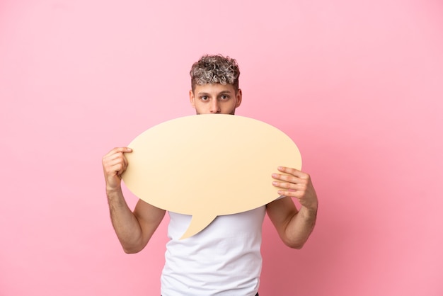 Jonge knappe blanke man geïsoleerd op roze achtergrond met een lege tekstballon die erachter verstopt zit