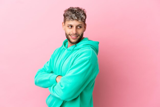 Jonge knappe blanke man geïsoleerd op roze achtergrond op zoek naar de kant en glimlachend