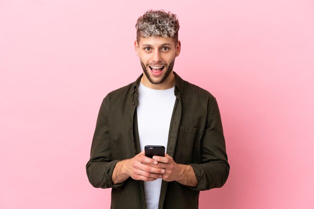 Jonge knappe blanke man geïsoleerd op roze achtergrond verrast en het verzenden van een bericht