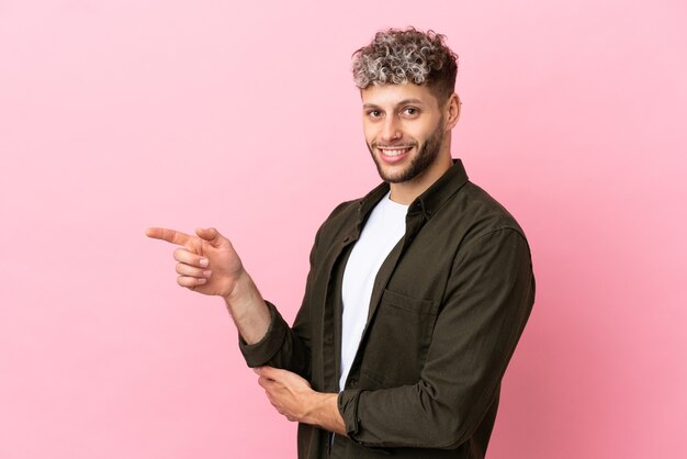 Jonge knappe blanke man geïsoleerd op roze achtergrond wijzende vinger naar de zijkant