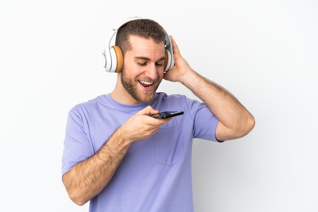 Jonge knappe blanke man geïsoleerd op wit muziek luisteren met een mobiele telefoon en zingen