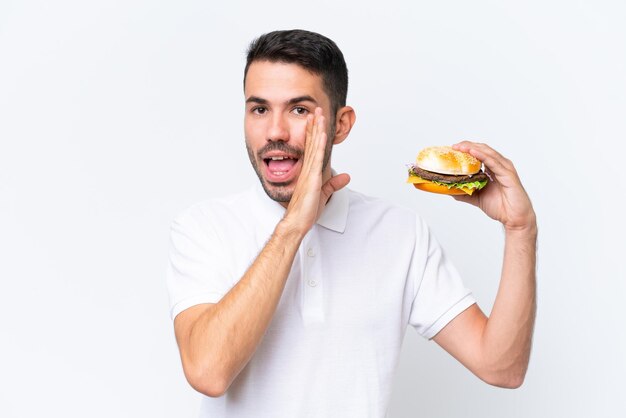 Jonge knappe blanke man met een hamburger over geïsoleerde achtergrond iets fluisterend
