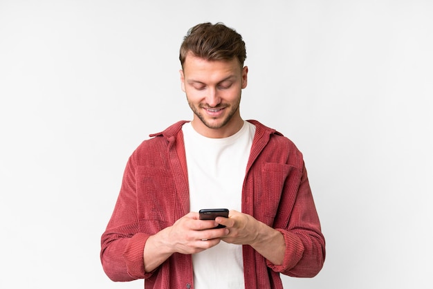 Jonge knappe blanke man op een geïsoleerde witte achtergrond die een bericht stuurt met zijn mobiele telefoon
