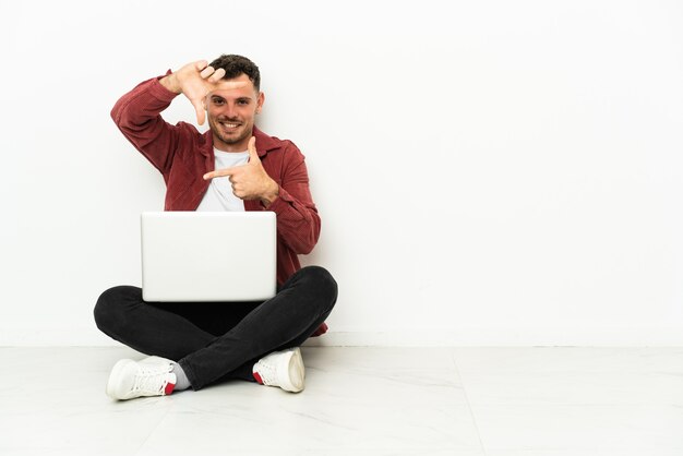 Jonge knappe blanke man sit-in op de vloer met laptop gericht gezicht. Framing symbool