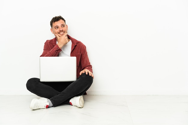 Jonge knappe blanke man sit-in op de vloer met laptop op zoek naar de zijkant