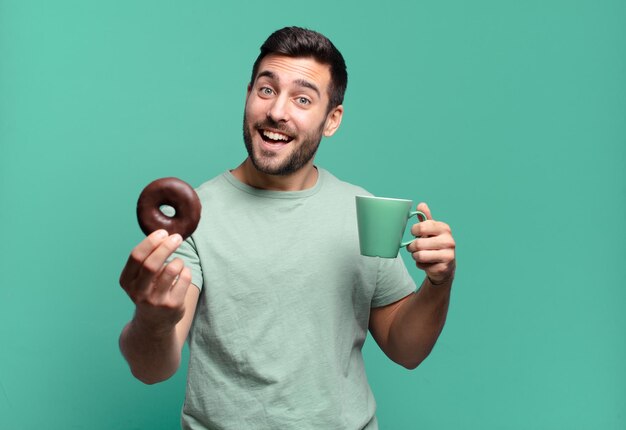Jonge knappe blonde man met een chocolade donut en een koffiekopje. ontbijt concept