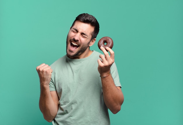 Jonge knappe blonde man met een chocolade donut. ontbijt concept