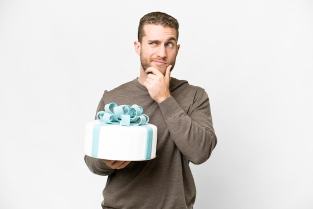 Jonge knappe blonde man met een grote cake over een geïsoleerde witte achtergrond die twijfels heeft en nadenkt