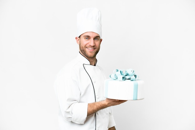 Jonge knappe blonde man met een grote cake over een geïsoleerde witte achtergrond die veel glimlacht