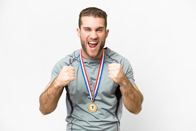 Jonge knappe blonde man met medailles over geïsoleerde witte achtergrond die een overwinning viert in de positie van winnaar