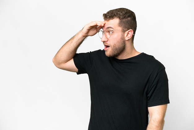 Jonge knappe blonde man op een geïsoleerde witte achtergrond met een verrassende uitdrukking terwijl hij naar de zijkant kijkt