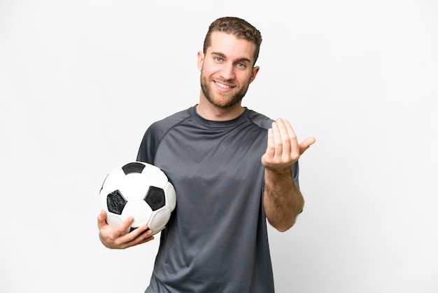 Jonge knappe blonde man over geïsoleerde witte achtergrond met voetbal en komend gebaar doen