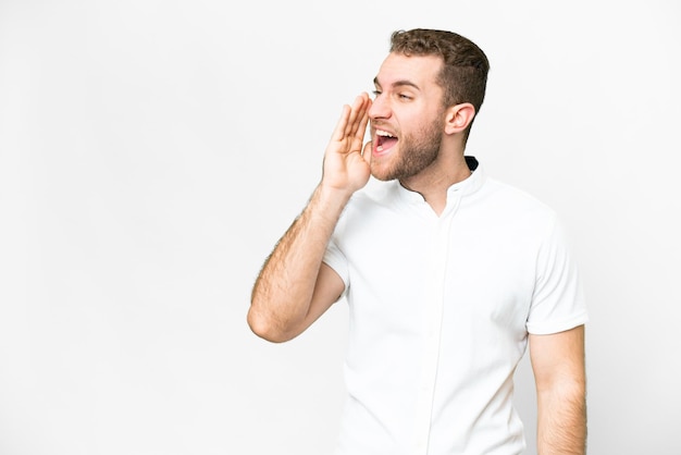 Jonge knappe blonde man over geïsoleerde witte achtergrond schreeuwend met mond wijd open naar de zijkant