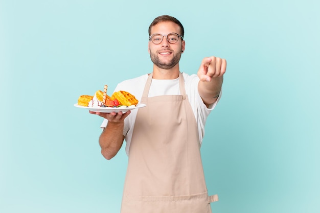 jonge knappe blonde man wijzend op de camera die jou kiest. wafels koken concept