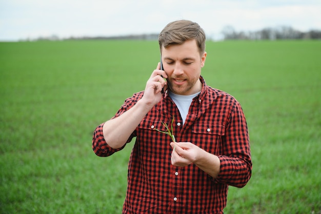 Jonge knappe boer die op landbouwgrond loopt en op mobiele telefoon praat