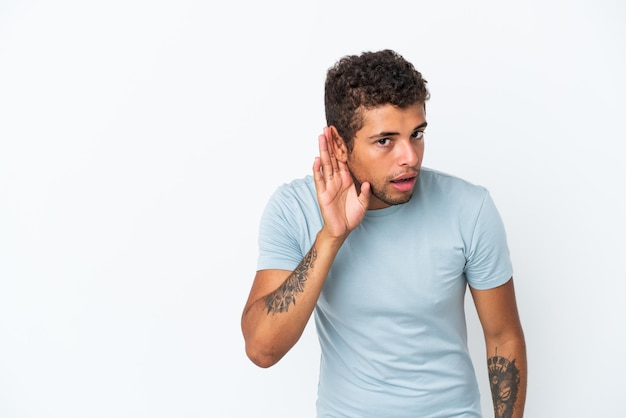 Jonge knappe Braziliaanse man geïsoleerd op een witte achtergrond luisteren naar iets door hand op het oor te leggen