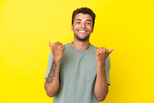 Jonge knappe Braziliaanse man geïsoleerd op gele achtergrond met duim omhoog gebaar en lachend