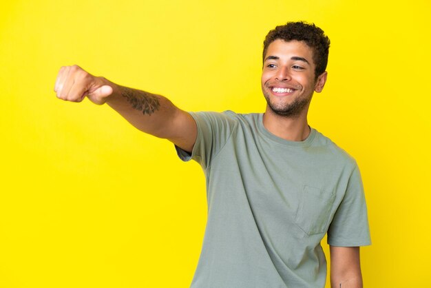 Jonge knappe Braziliaanse man geïsoleerd op gele achtergrond met een duim omhoog gebaar