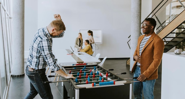 Jonge knappe casual multi-etnische zakenmensen die tafelvoetbal spelen en ontspannen op kantoor