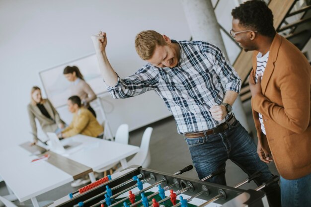 Jonge knappe casual multi-etnische zakenmensen die tafelvoetbal spelen en ontspannen op kantoor