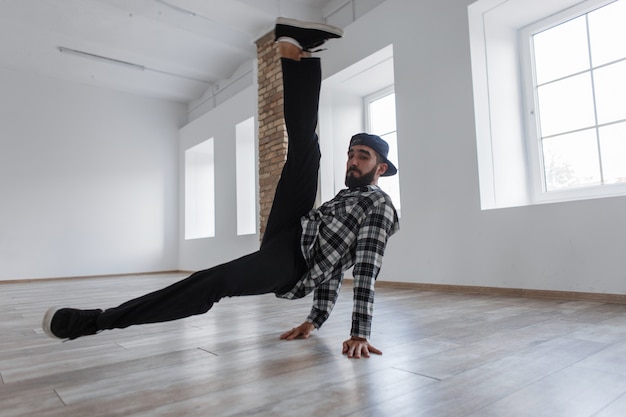 Jonge knappe danseres man met pet in shirt met sneakers dansen op handen in de studio