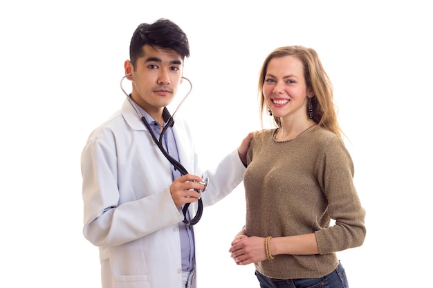 Jonge knappe dokter in witte jurk met stethoscoop luisteren naar de hartslag van jonge vrouw