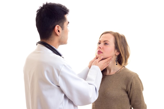 Jonge knappe dokter met donker haar in witte jurk met stethoscoop op zijn nek die jonge vrouw onderzoekt