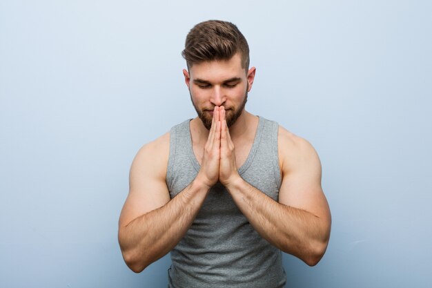 Jonge knappe fitness man hand in hand bidden in de buurt van mond, voelt zich zelfverzekerd.