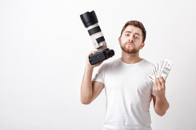 Jonge knappe fotograaf met een baard in een wit overhemd met een camera en honderd-dollarbiljetten. betaling voor de fotoshoot