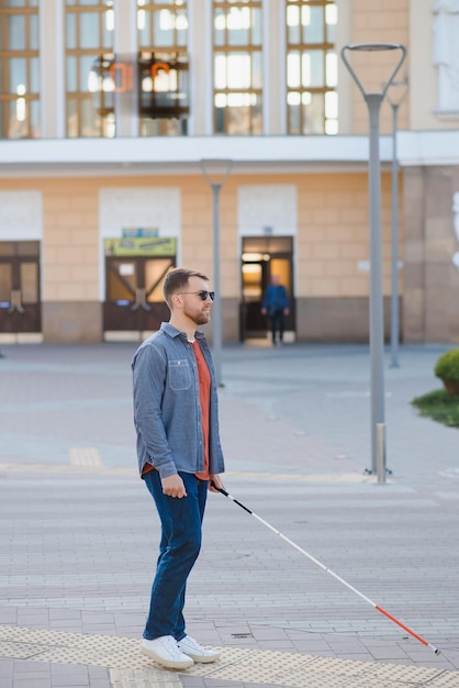 Foto jonge knappe geblindeerde man die met een stok in de stad loopt
