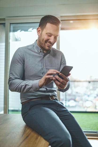 Jonge knappe gelukkige succesvolle ondernemer gebruikt smartphone op kantoor om een bericht te sms'en.