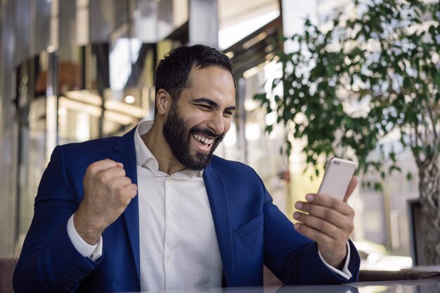 Jonge knappe handelaar vieringssucces gelukkige zakenman die mobiele telefoon houdt die goed nieuws leest